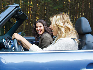 To unge kvinner i cabriolet som ler og smiler