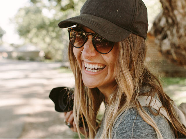 Kvinne med caps og solbriller ler og smiler.